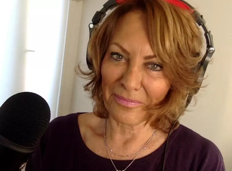 Viv looking at the camera. She is wearing headphones and is sat in front of a black microphone. She has golden, shoulder-length hair and is wearing a black top.