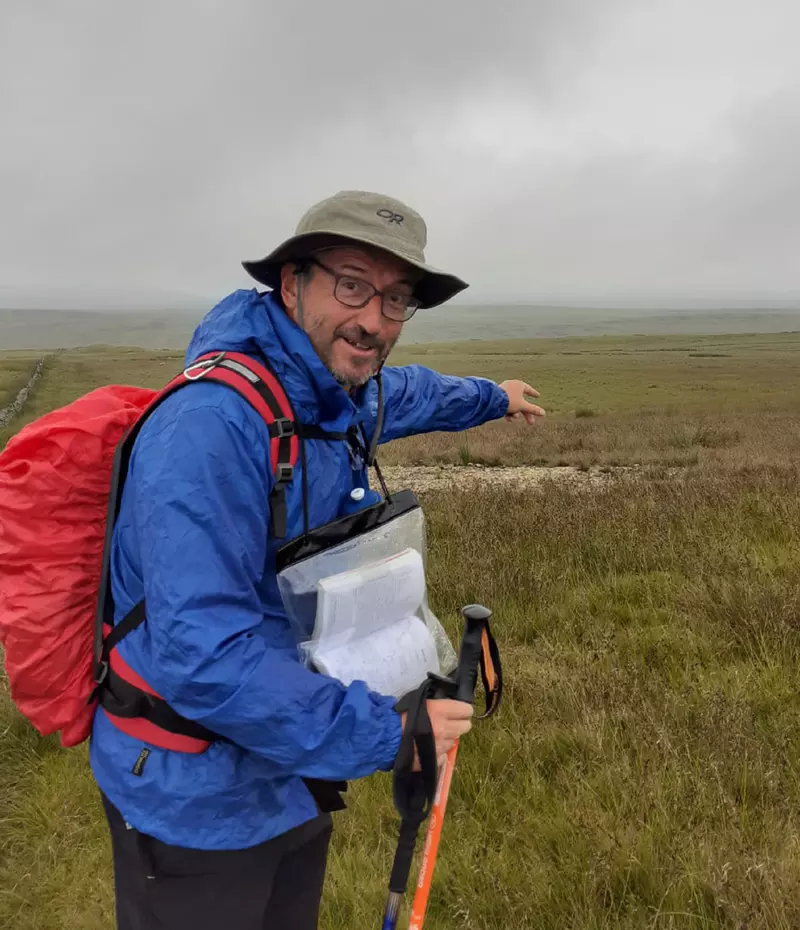 Karl on a hike. He wears a blue cagoul and has a red backpack. The sky is grey!