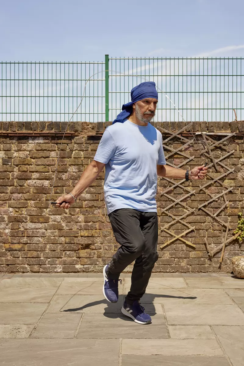 Jagdeep is skipping with a rope on a paved area. He is wearing black jogging bottoms with a light blue tshirt. His turban is blue.